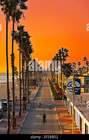 Tramonto sulla strada con turisti e aziende lungo la spiaggia, strada fiancheggiata da palme. Foto Stock