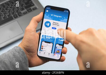 Kharkov, Ucraina - 9 marzo 2021: Mano dell'uomo che tiene Apple iPhone 12 con l'applicazione Telegram nel negozio, l'uomo che sta andando usare il social network per chattare Foto Stock