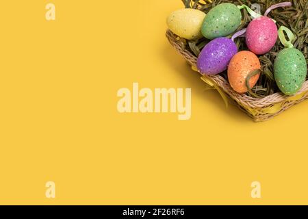 Uova colorate di Pasqua in un cestino isolato su uno sfondo giallo illuminante alla moda. Concetto di pasqua minimo. Carta di Pasqua con spazio per la copia del testo. Foto Stock