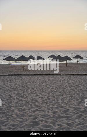 Spiaggia vuota al tramonto a Comporta, Portogallo con ombrelloni estivi di paglia Foto Stock