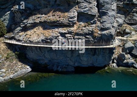 Ciclisti sul ponte a sbalzo sulla pista ciclabile del lago Dunstan e sul lago Dunstan, vicino a Cromwell, Central Otago, South Island, Nuova Zelanda Foto Stock