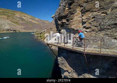 Ciclisti sul ponte a sbalzo sulla pista ciclabile del lago Dunstan e sul lago Dunstan, vicino a Cromwell, Central Otago, South Island, Nuova Zelanda Foto Stock