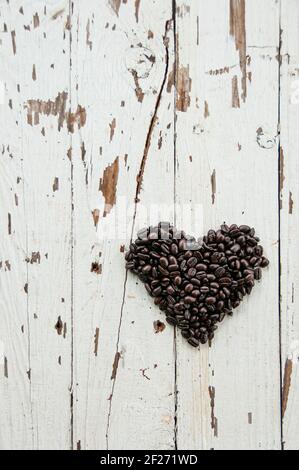 Vista dall'alto del simbolo del cuore fatto di chicchi di caffè tostati su un rustico tavolo di legno color bianco. Chicchi di caffè a forma di cuore. Concetto creativo piatto per l'amore Foto Stock