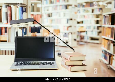 Studiare all'università: Computer portatile su una scrivania di legno, mucchio di libri e libri in background sfocato Foto Stock