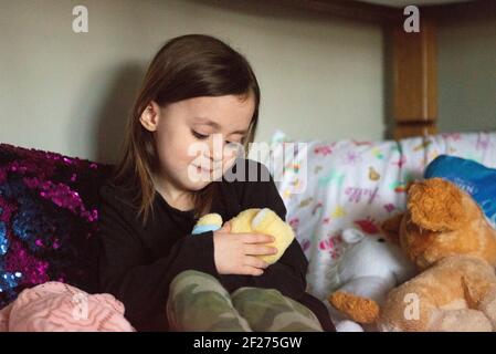 Bambina seduta sul letto che tiene l'animale farcito. Foto Stock