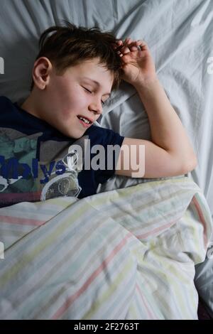 ragazzo che slitta sorridendo nel suo letto di mattina Foto Stock