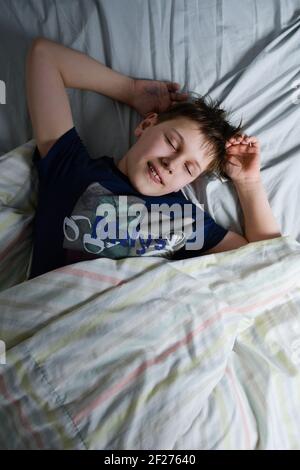 ragazzo sorridente sdormì nel letto sotto la coperta Foto Stock