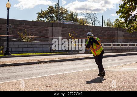 Si vede un operatore di costruzioni che indossa un completo equipaggiamento protettivo che include casco, gilet riflettente, stivali, guanti, occhiali da sole e maschera facciale contro COVID-19 Foto Stock