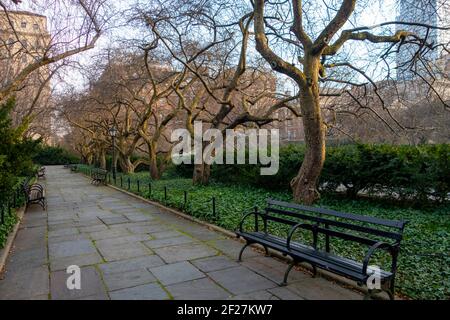 parco cittadino con banchina rettangolare con panchine cespugli sempreverdi e perenne coperta di terra frondosa e alberi di caduta tardiva senza frondolo Foto Stock