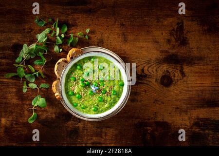 Zuppa verde vegana, sparata dall'alto con toast e menta su uno sfondo di legno rustico scuro Foto Stock