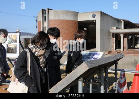 Ishinomaki, Giappone. 9 marzo 2021. I visitatori guardano le foto della scuola prima del disastro esposto alle rovine della scuola elementare di Okawa a Ishinomaki, Giappone, il 9 marzo 2021. Una scuola elementare pubblica nella prefettura di Miyagi ha perso più di 80 vite nello tsunami a seguito del terremoto del 2011 marzo nel Giappone nordorientale. Dieci anni dopo, le rovine dell'edificio scolastico raccontano ancora l'inimmaginabile tragedia della calamità. PER ANDARE CON 'Feature: 10 anni dopo, la scuola giapponese di tsunami-colpito ancora dice tragedia inimmaginabile' Credit: Du Xiaoyi/Xinhua/Alamy Live News Foto Stock