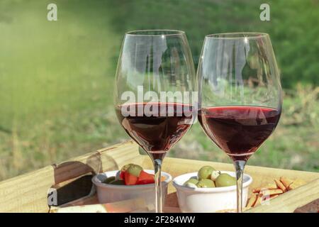 Un pic-nic con due bicchieri di vino rosso, con verde sfocato sullo sfondo Foto Stock