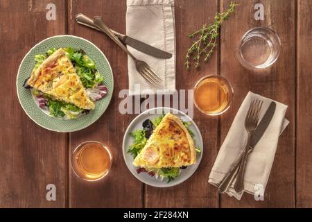 Fette di quiche francesi con salmone, con foglie di insalata verde, timo e vino bianco, sparate dall'alto su un rustico backgro di legno Foto Stock