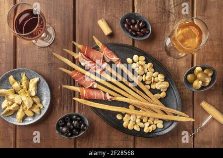 Antipasti all'italiana. Grissini, prosciutto di Parma, mandorle, olive e vino al buio su un rustico sfondo di legno Foto Stock