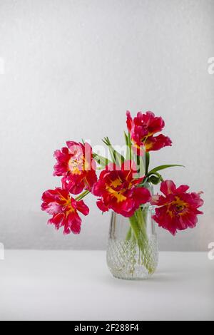Vaso in vetro con bouquet di bei tulipani su fondo muratura in mattoni. Tulipano riccamente Foto Stock