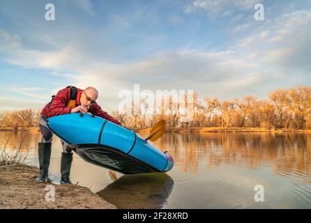 il paddler maschio anziano sta aggiungendo aria ad un packraft gonfiabile su una riva del lago in uno scenario primaverile a nord Colorado Foto Stock