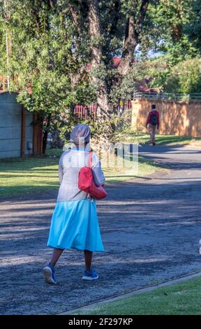 Johannesburg, Sud Africa - una donna nera non identificata con una borsa rossa brillante cammina lungo una strada pubblica Foto Stock