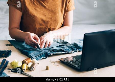 Una donna è impegnata nella formazione online e guarda le lezioni di cucito su un computer portatile. Concetto di apprendimento online alla moda che prende corsi a casa. Necessità casalinga Foto Stock