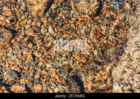 Piccole pietre, ciottoli, sotto acqua limpida in giornata di sole Foto Stock