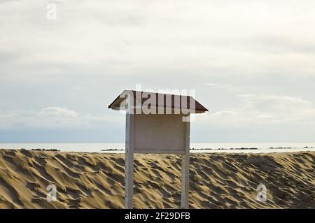 Cartello in legno sulla spiaggia di fronte ad una duna di sabbia sulla costa mediterranea (Pesaro, Italia, Europa) Foto Stock