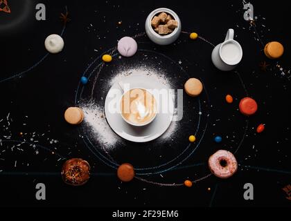 tazza di caffè, ciambelle, macaron, zucchero, caraffa per crema di latte e torte su sfondo nero assomiglia a un sistema di caffè Foto Stock