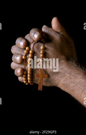 Mano di preghiera di un vecchio cattolico indiano con rosario di legno isolato su uno sfondo nero chiaro. Foto Stock