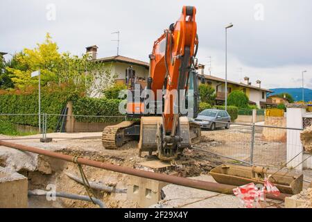 Una trincea di pozzo di fogna & un escavatore cingolato con un piattaforma rotante e cingolo caterpillar continuo su una fogna Cantiere di sostituzione in NE Italia Foto Stock