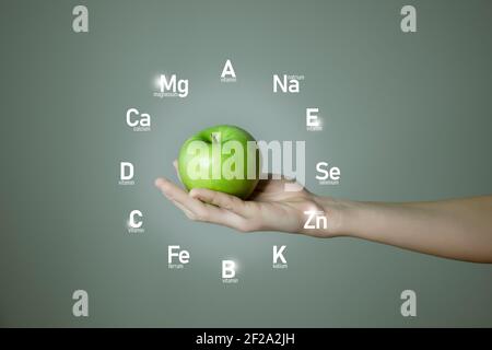 Donna`s mano che tiene la mela verde, icone microelementi in forma di cerchio a forma di clockface su sfondo grigio. Modello di concetto perdita di peso per la progettazione del prodotto. Foto Stock