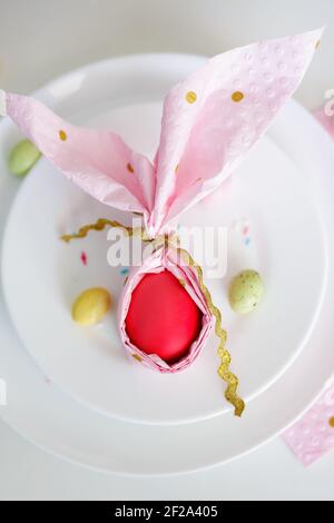 concetto di festa di primavera - vista dall'alto del piatto con pasqua uovo avvolto in tovagliolo rosa a forma di orecchie conigliate Foto Stock