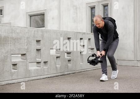 concetto di filmmaking, hobby e creatività - videografo maschile professionista che scatta video utilizzando la moderna fotocamera dslr su gimbal a 3 assi su cemento Foto Stock