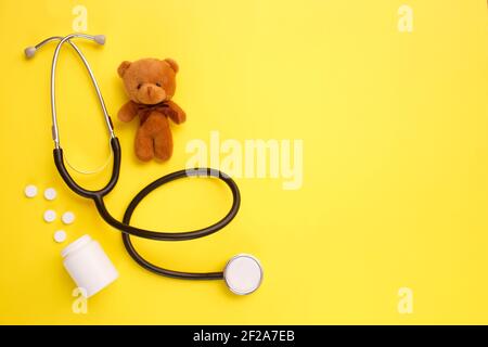 Orsacchiotto giocattolo per bambini con stetoscopio su sfondo giallo con spazio per la copia. Concetto di salute dei bambini. Vista dall'alto, disposizione piatta Foto Stock