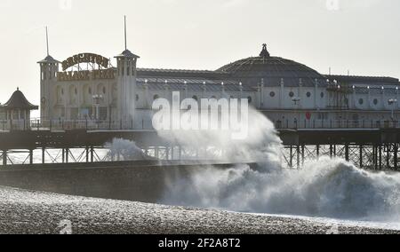 Brighton UK 11 marzo 2021 - le onde si schiantano sulla spiaggia dal molo di Brighton Palace mentre il tempo tempestoso batte oggi la costa meridionale : Credit Simon Dack / Alamy Live News Foto Stock