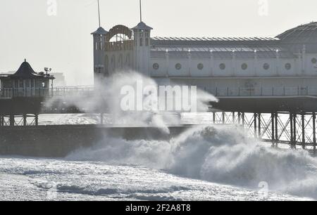Brighton UK 11 marzo 2021 - le onde si schiantano sul lungomare dal molo di Brighton Palace mentre il tempo tempestoso batte oggi la costa meridionale : Credit Simon Dack / Alamy Live News Foto Stock