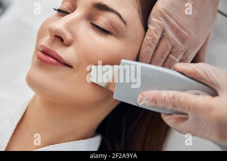 Cosmetologist mani che pulisce la faccia della donna con lo scrubber ultrasonico Foto Stock
