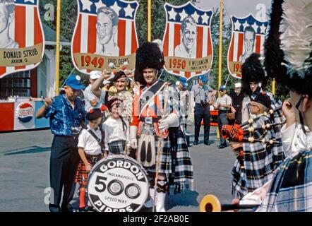 Una band scozzese di pipe al circuito di Derby Downs, Akron, Ohio, USA nel 1965. Il locale è stato il circuito di casa del ‘All American SOAP Box Derby’ da quando è stato costruito come progetto di Works Progress Administration (WPA) negli anni trenta. I membri della band provengono dai Gordon Pipers dell'Indianapolis 500 Speedway. Le tradizioni abbondano con i famosi vincitori precedenti delle gare mostrate sui banner, tra cui Fred Derks (1949) e Harold ‘Butch’ Williamson (1950). Questa immagine è tratta da un vecchio lucido a colori americano amatoriale Kodak – una fotografia d'epoca degli anni '60. Foto Stock