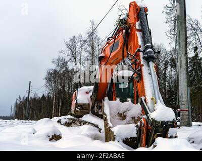 Grande escavatore arancione coperto di neve. Abbandonati non funzionanti attrezzature di costruzione rotte. Foto Stock