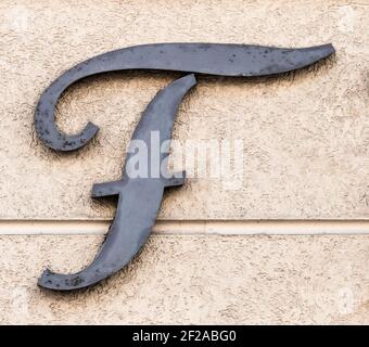 Lettera F grigia in metallo su una parete della casa color sabbia Foto Stock