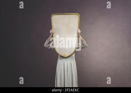 la donna si nasconde tenendo uno specchio davanti al viso; concetto di introspezione Foto Stock