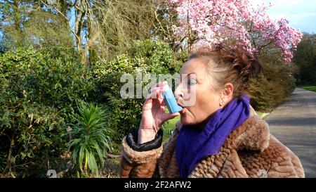 Donna matura che usa un inalatore in un giardino - John Gollop Foto Stock