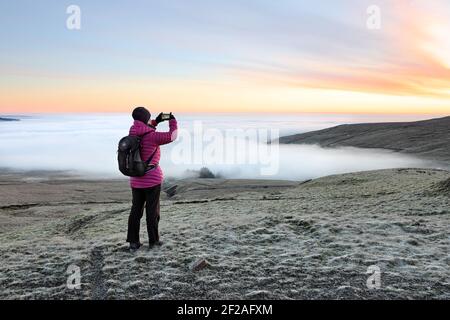 Un camminatore che fotografa un cielo colorato sopra la nuvola ha riempito le valli a Dawn nel Nord Pennines, Weardale, contea di Durham, Regno Unito Foto Stock