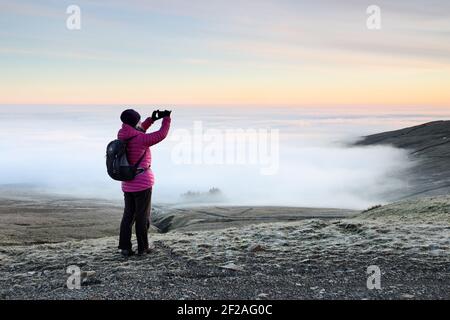 Una Walker che fotografa una valle riempita di nuvola sul suo telefono a Dawn nel Nord Pennines, Weardale, contea Durham, Regno Unito Foto Stock
