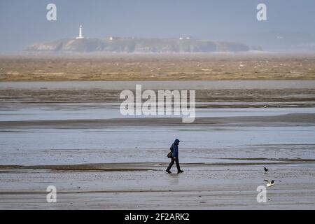 Un camminatore sulla spiaggia di Weston-super-Mare, Somerset. Sono state emesse avvertenze di sicurezza per le zone costiere dell'Inghilterra e del Galles, come previsto vento fino a 70 mph. Data immagine: Giovedì 11 marzo 2021. Foto Stock