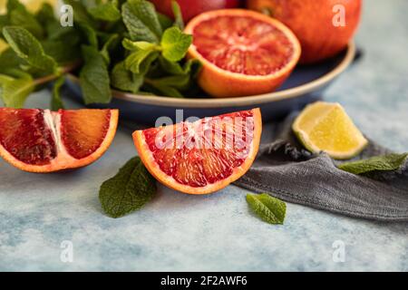 Arance siciliane rosse con lime e menta su sfondo blu. Agrumi interi e tagliati a fette. Messa a fuoco selettiva. Foto Stock