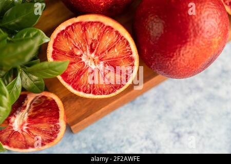 Fette e intere arance succose succose siciliane mature su tagliere di legno con menta, fondo di cemento blu. Messa a fuoco selettiva. Vista dall'alto. Foto Stock