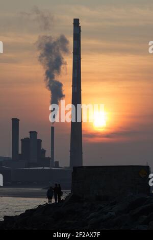 Poolbeg Power centrale fumo camini al tramonto, cielo arancione, foto nuvolosa scattata contro il sole, sagome Foto Stock