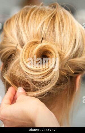 Primo piano di acconciatore femminile styling capelli biondi di a. giovane donna in un salone di bellezza Foto Stock