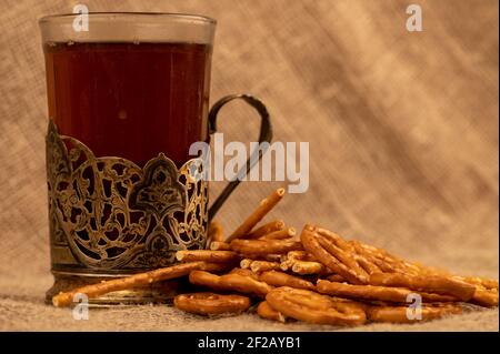 Grissini salati e pretzel salati sfusi e un bicchiere di tè in un portabicchieri sul tavolo. Messa a fuoco selettiva in primo piano. Foto Stock