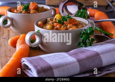 Deliziosa zuppa di legumi alle verdure con carne sminuzzata in zuppa rustica tazze servite su tavolo di legno Foto Stock