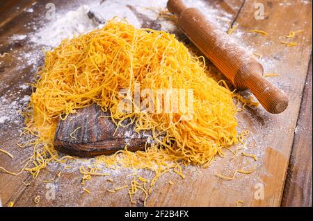 Tagliatelle . Capelli d'angelo di nome italiano tradizionale (capellini d'angeli). Donna che cucinava pasta all'uovo italiana, fatta in casa e fresca in farina su un tavolo da taglio. Foto Stock