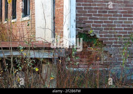 Primo piano di un muro di mattoni danneggiato in un vecchio edificio abbandonato, dove lo strato esterno di mattoni è caduto via, rivelando un altro strato di mattoni. Foto Stock